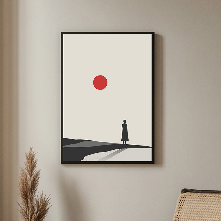 Framed minimalist poster of a lone figure standing in a desert landscape with a red sun above, displayed on a beige wall with natural decor elements nearby.