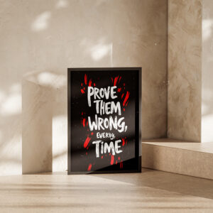 Motivational poster in a black frame with the quote 'Prove Them Wrong, Every Time' displayed in bold white and red text, leaning against a minimalist concrete wall