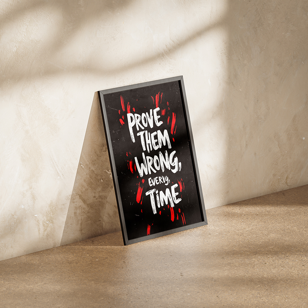 Motivational poster in a black frame with the quote 'Prove Them Wrong, Every Time' displayed in bold white and red text, leaning against a minimalist concrete wall