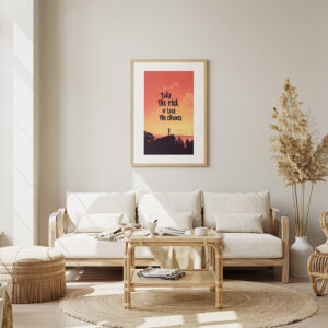 Framed poster with the motivational quote 'Take the Risk or Lose the Chance' in a sunset-themed design, displayed in a cozy, boho-style living room with neutral tones.